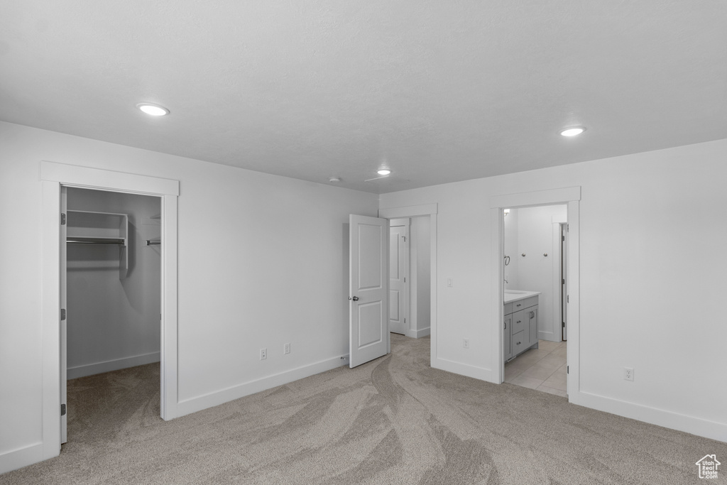 Unfurnished bedroom featuring connected bathroom, a walk in closet, light colored carpet, and a closet