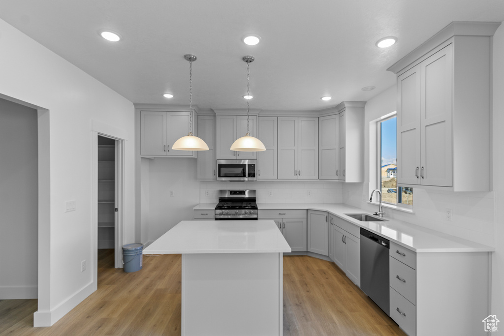 Kitchen featuring sink, hanging light fixtures, light wood-type flooring, a kitchen island, and stainless steel appliances