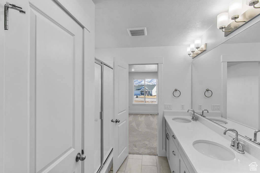 Bathroom featuring vanity, a shower with shower door, tile patterned flooring, and a textured ceiling