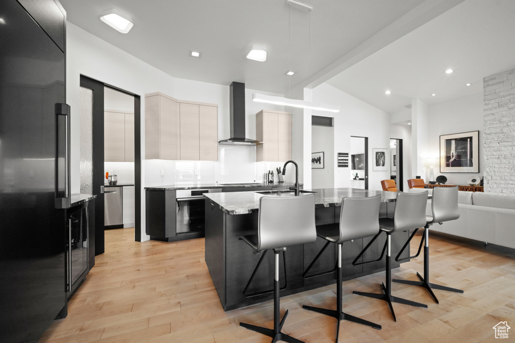 Kitchen with wall chimney exhaust hood, sink, a center island with sink, appliances with stainless steel finishes, and a kitchen breakfast bar