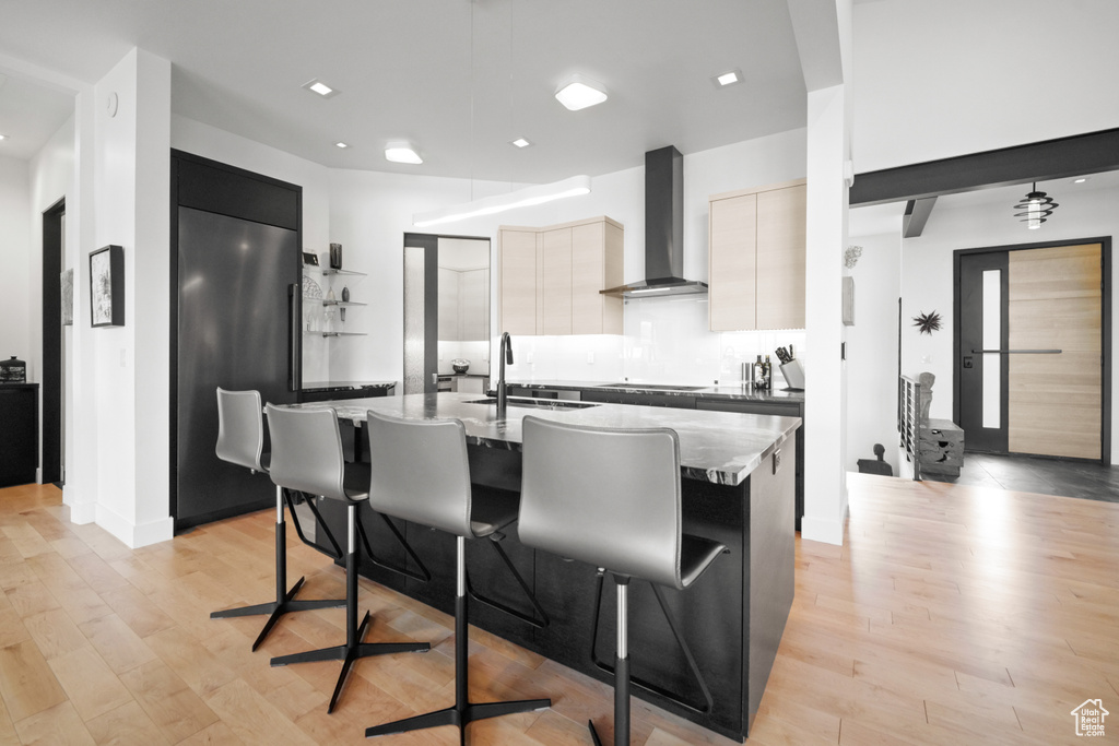 Kitchen with wall chimney range hood, sink, a breakfast bar, paneled fridge, and an island with sink