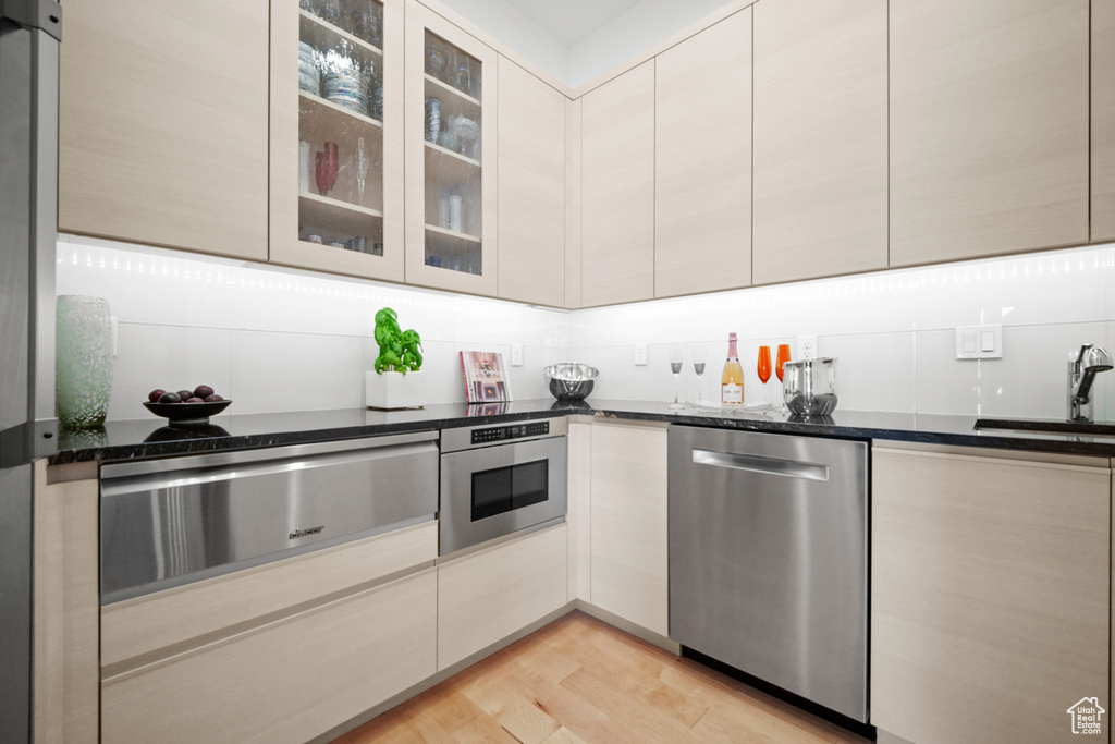 Kitchen featuring stainless steel appliances, sink, light wood-type flooring, and dark stone counters