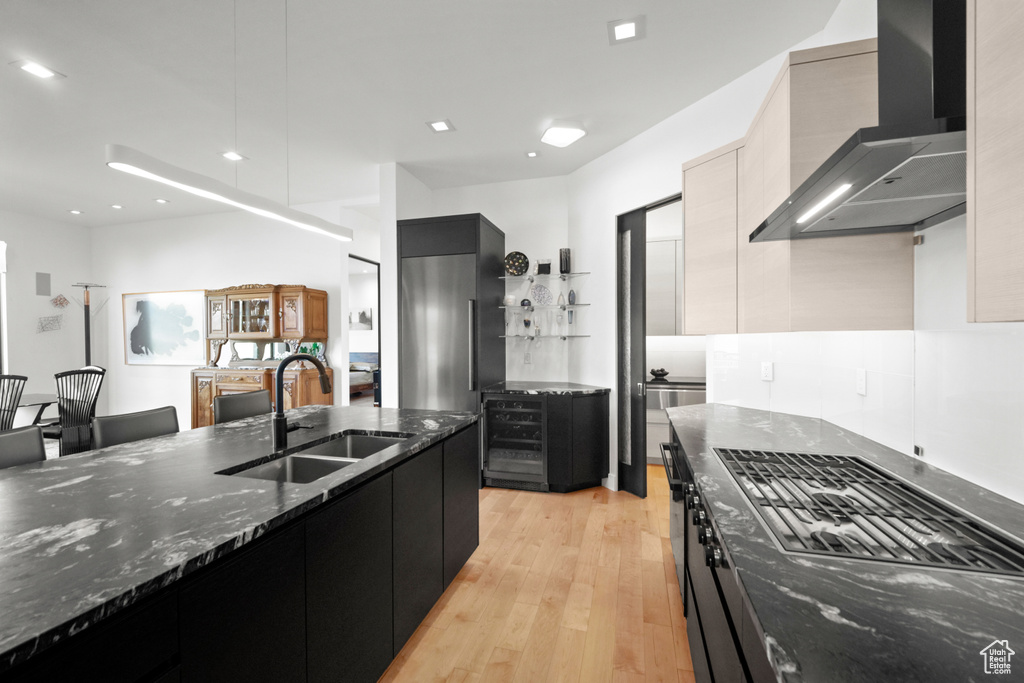 Kitchen featuring dark stone counters, sink, light hardwood / wood-style flooring, and wall chimney range hood