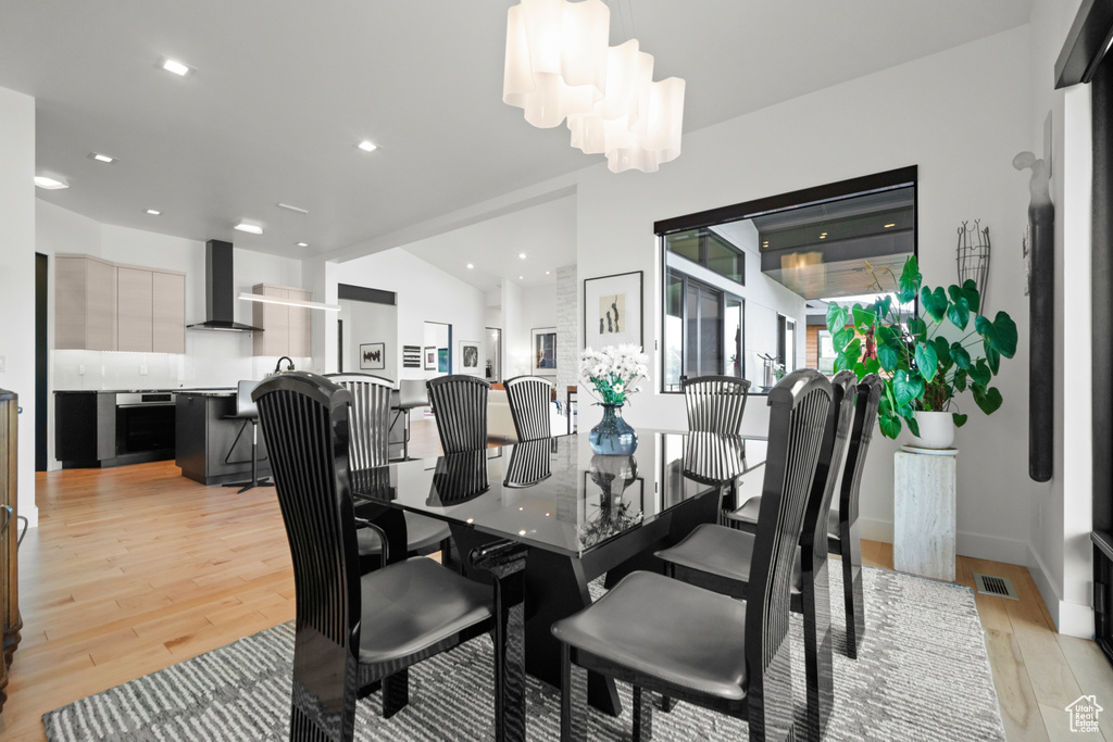 Dining room with a notable chandelier, vaulted ceiling, and light wood-type flooring