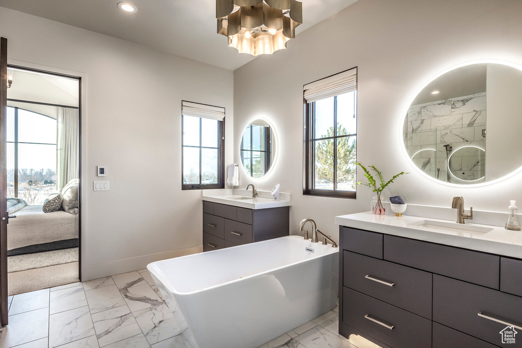 Ensuite bathroom with marble finish flooring, a soaking tub, two vanities, a chandelier, and recessed lighting