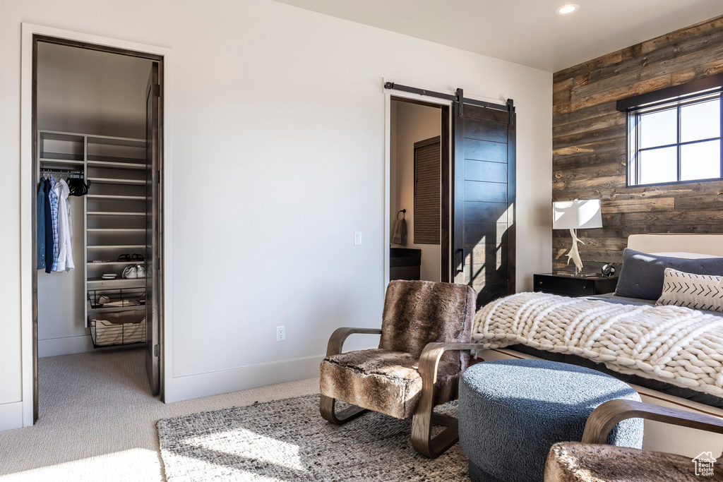 Bedroom with a barn door, a walk in closet, carpet floors, a closet, and wooden walls