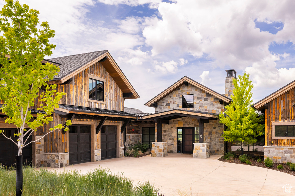 View of front facade with an attached garage, driveway, stone siding, and a chimney