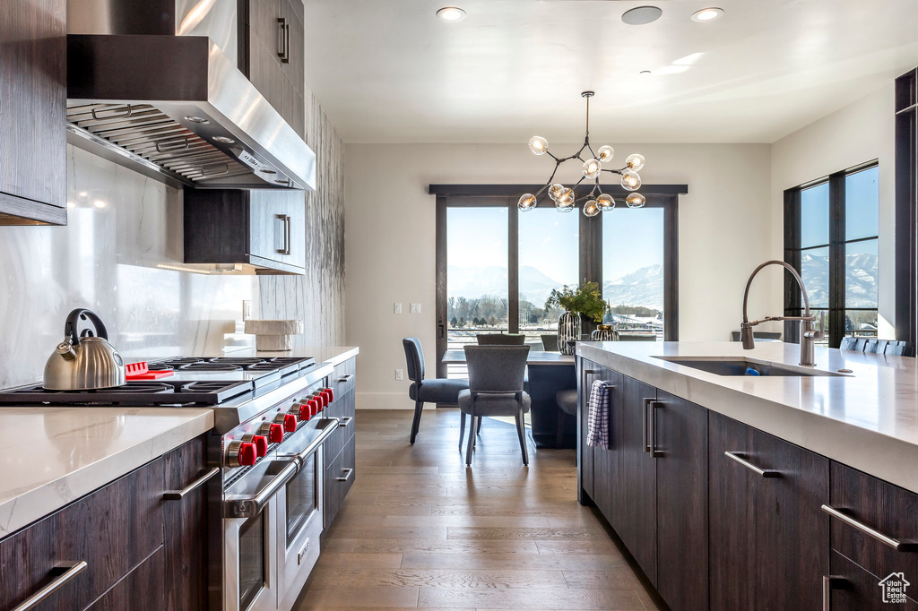 Kitchen with double oven range, wall chimney exhaust hood, a sink, light countertops, and dark brown cabinets
