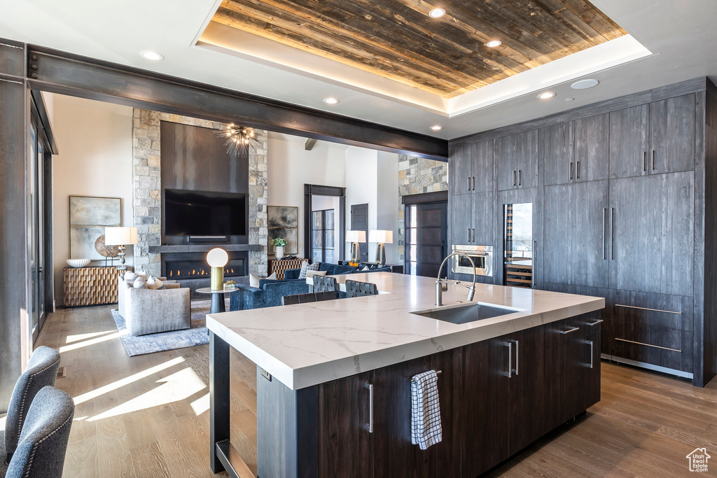 Kitchen with a tray ceiling, a sink, a kitchen island with sink, wood ceiling, and dark wood-type flooring