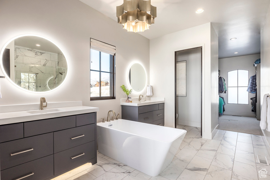 Bathroom featuring marble look tile flooring, a freestanding tub, two vanities, a chandelier, and a walk in shower
