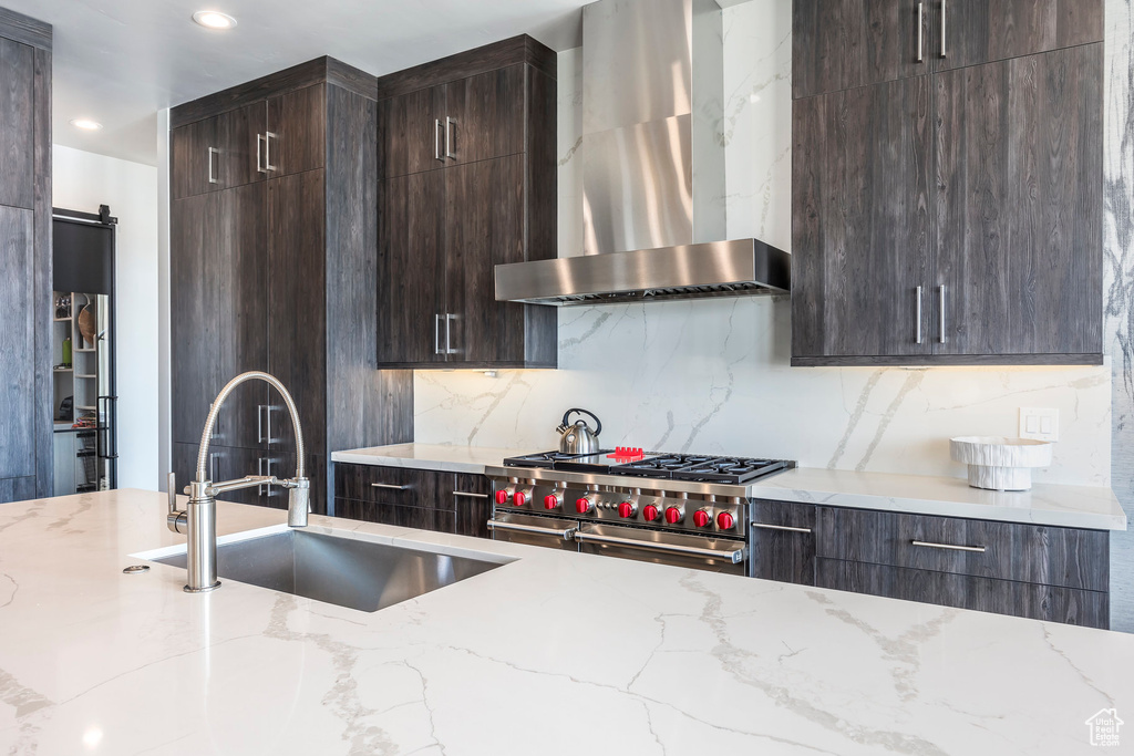 Kitchen featuring wall chimney exhaust hood, a sink, high end stainless steel range, dark brown cabinetry, and tasteful backsplash