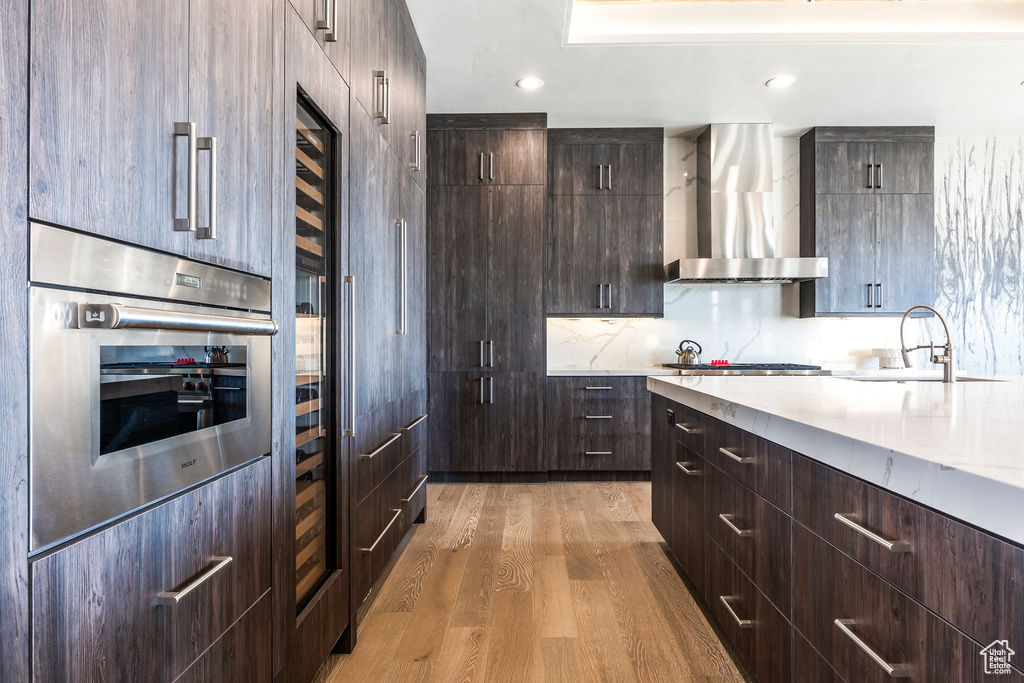 Kitchen featuring wall chimney range hood, modern cabinets, a sink, stainless steel appliances, and recessed lighting