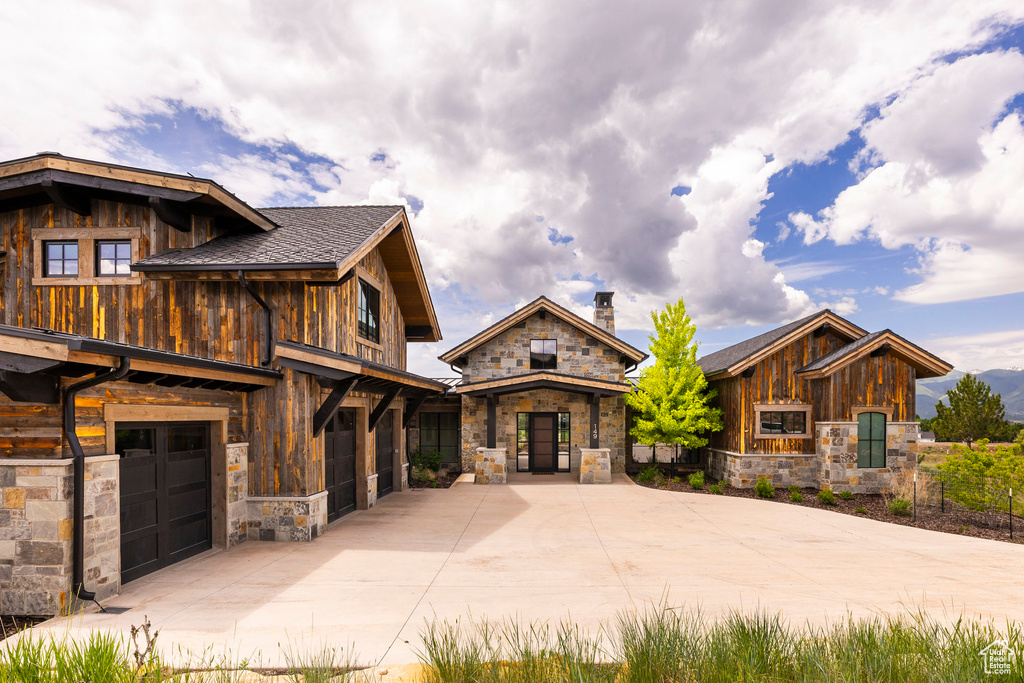 View of front facade with stone siding, driveway, a garage, and a chimney