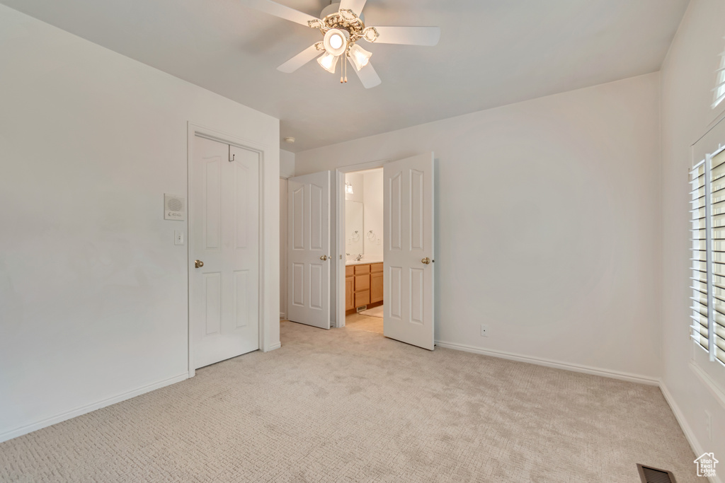 Unfurnished bedroom featuring light colored carpet, baseboards, connected bathroom, and a ceiling fan