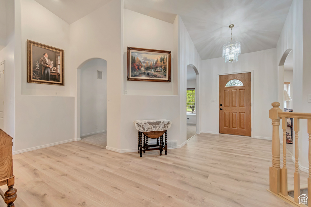 Foyer featuring arched walkways, wood finished floors, baseboards, a chandelier, and high vaulted ceiling