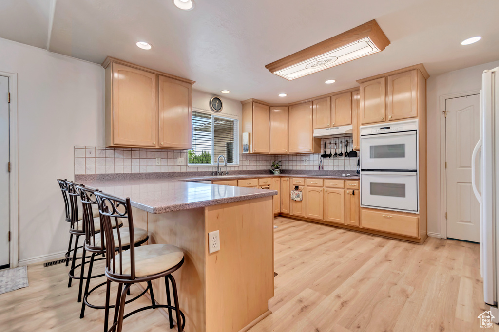 Kitchen with light brown cabinets, white appliances, a peninsula, a kitchen bar, and light wood-type flooring