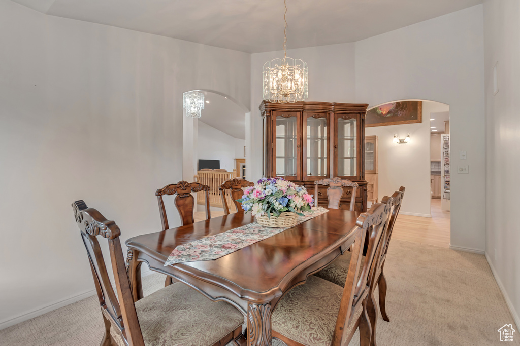 Dining area with arched walkways, light colored carpet, a chandelier, and baseboards