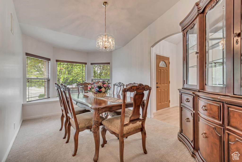 Dining room featuring arched walkways, a chandelier, light colored carpet, and baseboards