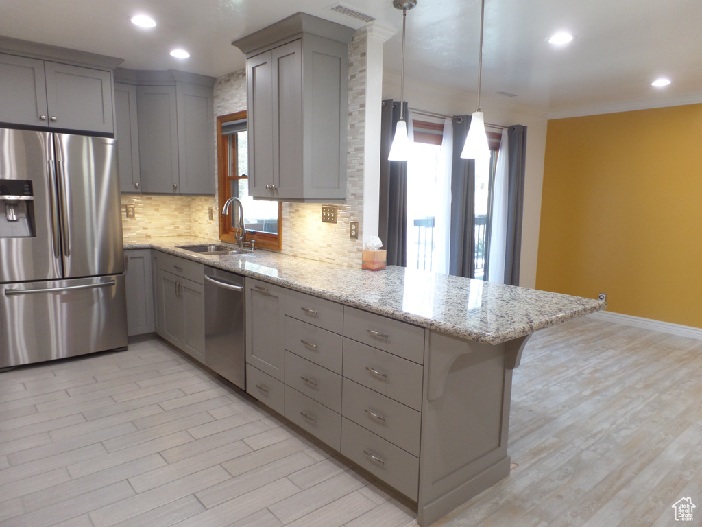 Kitchen with sink, light stone counters, hanging light fixtures, appliances with stainless steel finishes, and kitchen peninsula