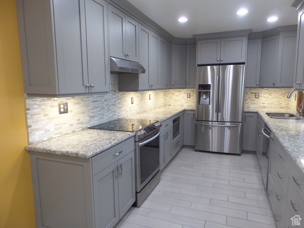 Kitchen with gray cabinets, light stone countertops, appliances with stainless steel finishes, and sink