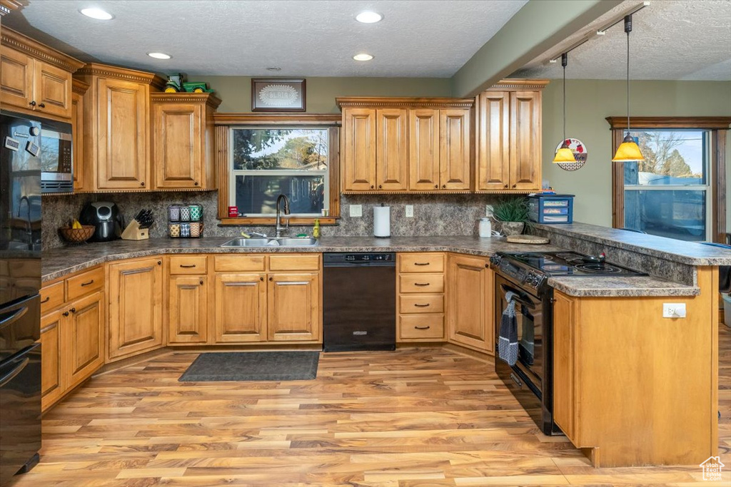 Kitchen featuring sink, light hardwood / wood-style flooring, hanging light fixtures, kitchen peninsula, and black appliances