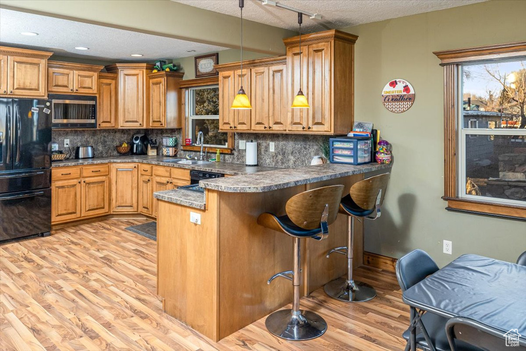 Kitchen featuring pendant lighting, black appliances, kitchen peninsula, a textured ceiling, and light hardwood / wood-style flooring