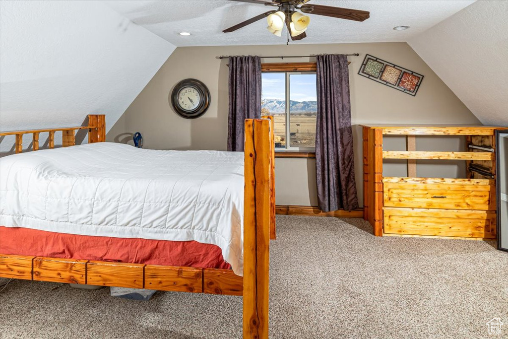 Bedroom with lofted ceiling, a textured ceiling, ceiling fan, and carpet