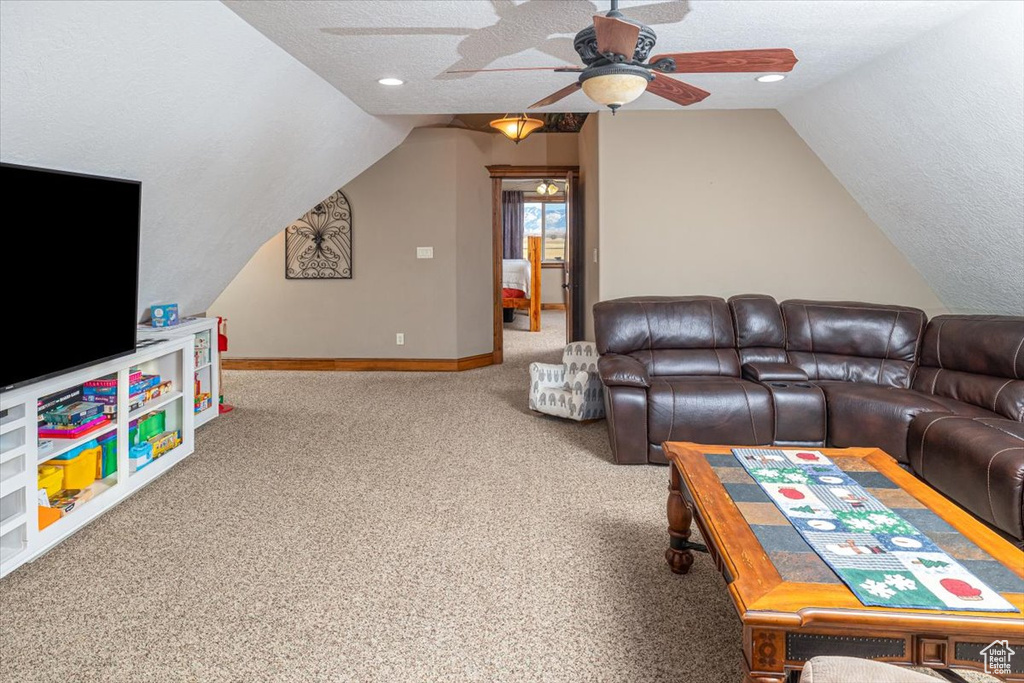 Living room with ceiling fan, lofted ceiling, carpet flooring, and a textured ceiling