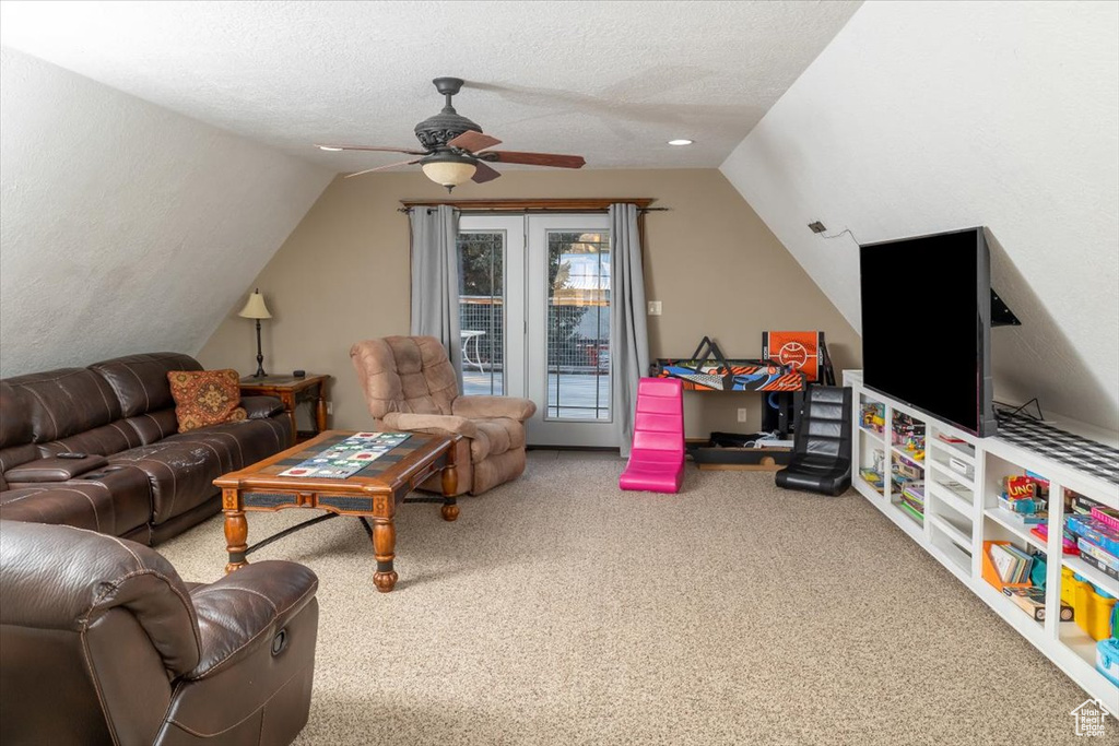 Living room featuring ceiling fan, lofted ceiling, carpet flooring, and a textured ceiling