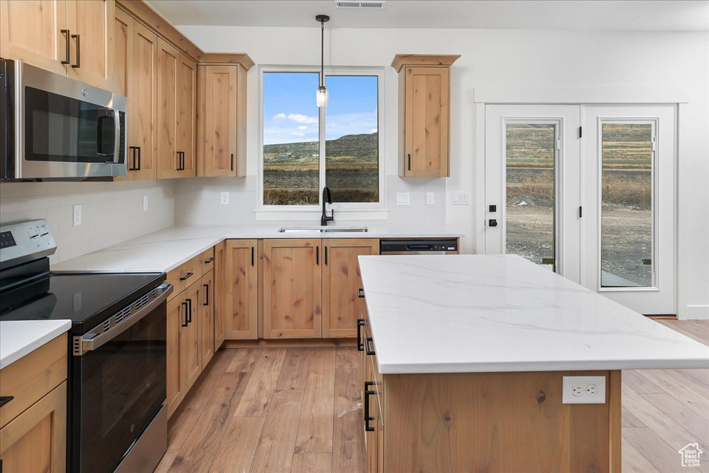 Kitchen with sink, decorative light fixtures, stainless steel appliances, and light hardwood / wood-style floors