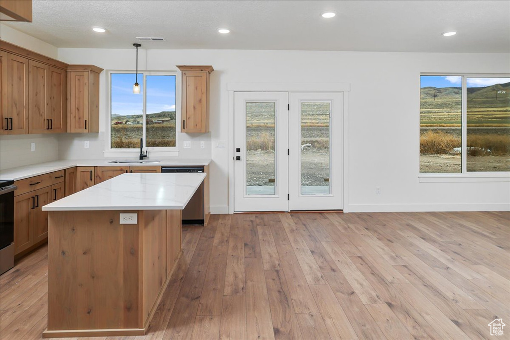 Kitchen with light stone counters, a center island, light hardwood / wood-style flooring, dishwasher, and pendant lighting