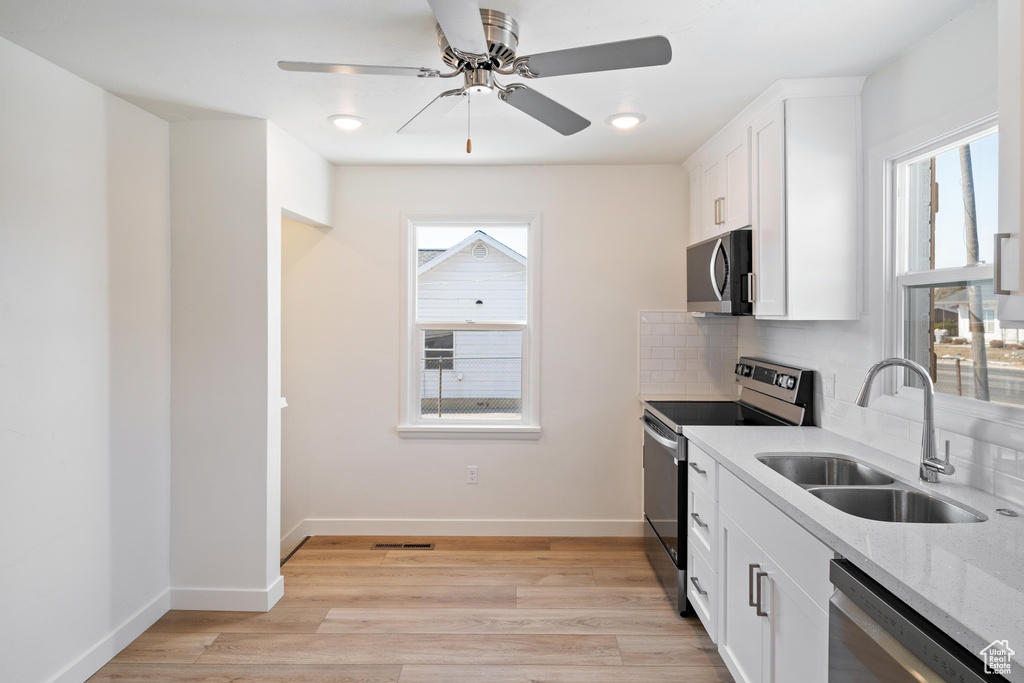 Kitchen featuring sink, tasteful backsplash, light wood-type flooring, appliances with stainless steel finishes, and white cabinets