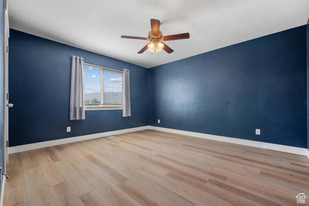 Empty room with a ceiling fan, wood finished floors, baseboards, and a textured ceiling