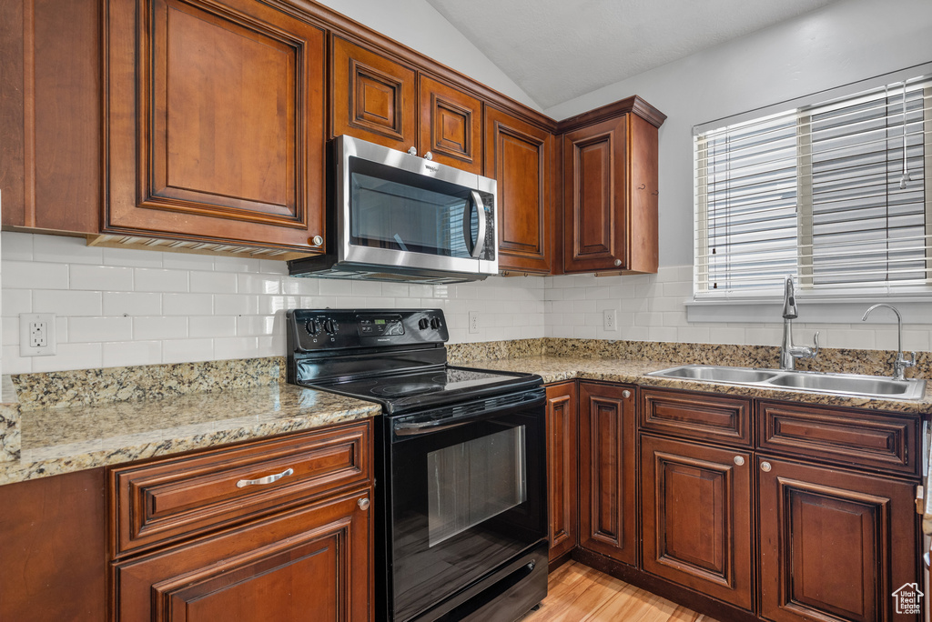 Kitchen with stainless steel microwave, black range with electric cooktop, a sink, lofted ceiling, and decorative backsplash