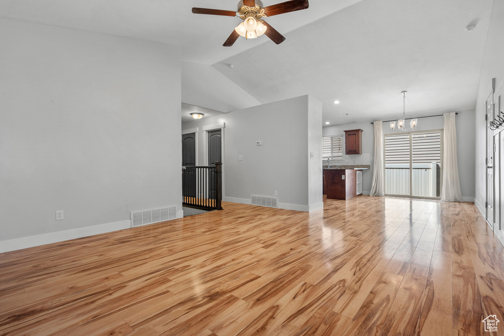 Unfurnished living room featuring a chandelier, light wood-style floors, ceiling fan, lofted ceiling, and baseboards