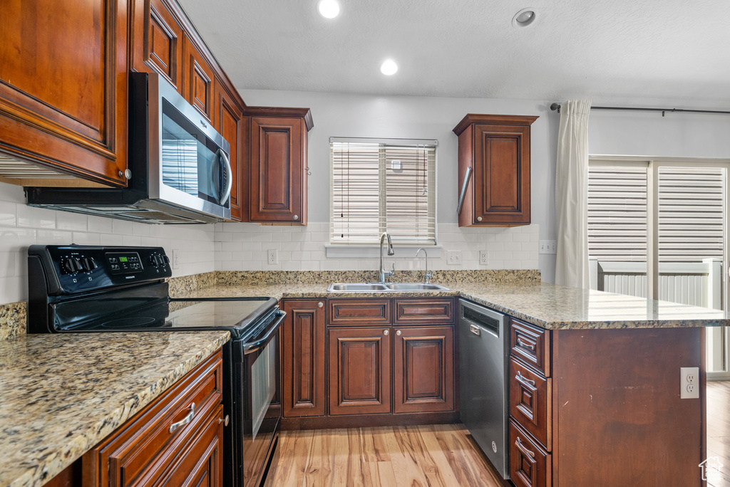 Kitchen with stainless steel appliances, a sink, a peninsula, light wood-type flooring, and light stone countertops