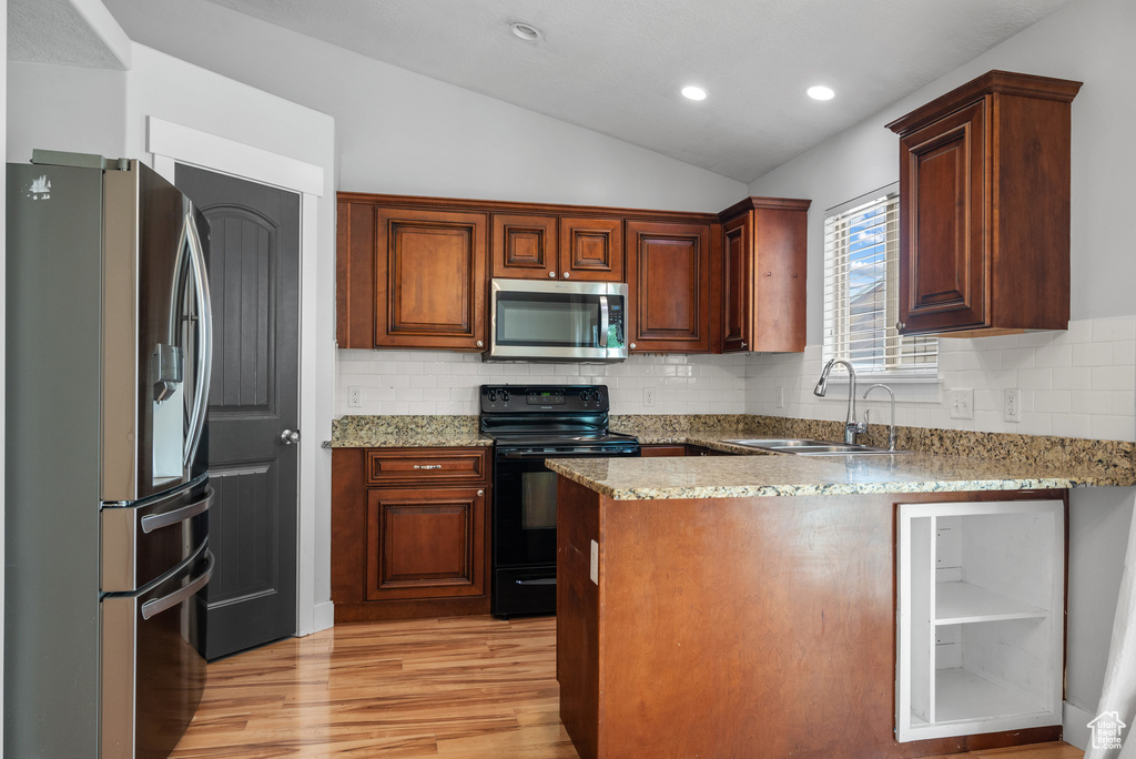 Kitchen featuring stainless steel appliances, a sink, vaulted ceiling, a peninsula, and light wood finished floors