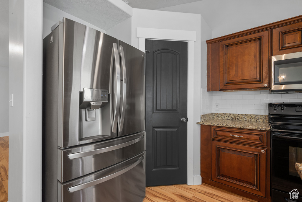 Kitchen featuring appliances with stainless steel finishes, light stone counters, light wood-style flooring, and decorative backsplash