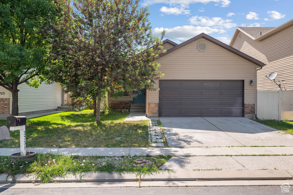 View of front of home with an attached garage, driveway, a front yard, and stone siding