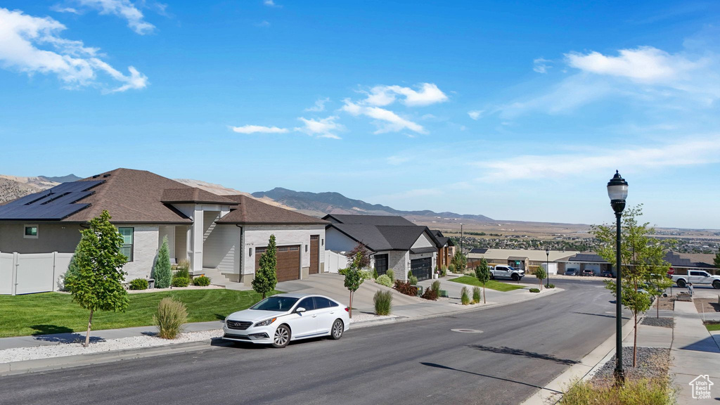 View of asphalt road featuring street lights, a mountain view, a residential view, and curbs