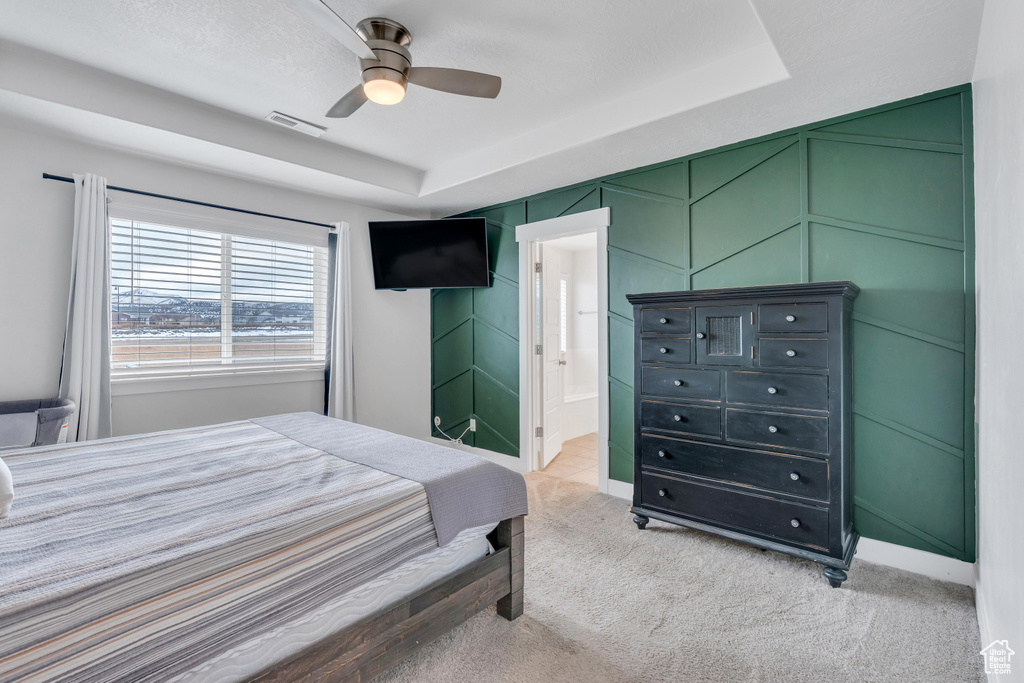 Bedroom with ensuite bathroom, light colored carpet, and ceiling fan