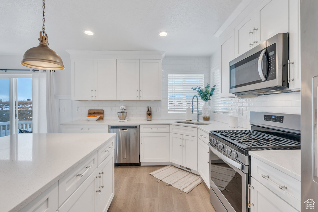 Kitchen featuring sink, light hardwood / wood-style flooring, hanging light fixtures, stainless steel appliances, and white cabinets