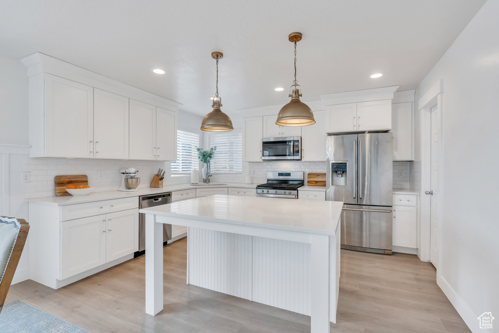 Kitchen with a kitchen island, appliances with stainless steel finishes, decorative light fixtures, white cabinetry, and light hardwood / wood-style floors