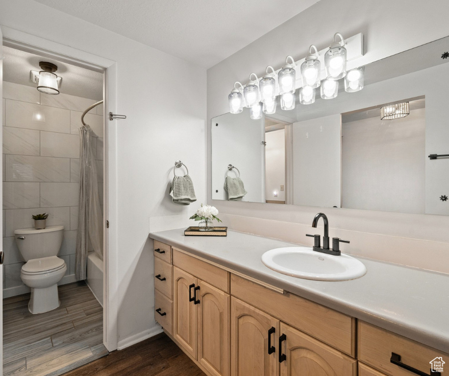 Bathroom featuring wood finished floors, vanity, toilet, shower / bath combination with curtain, and baseboards