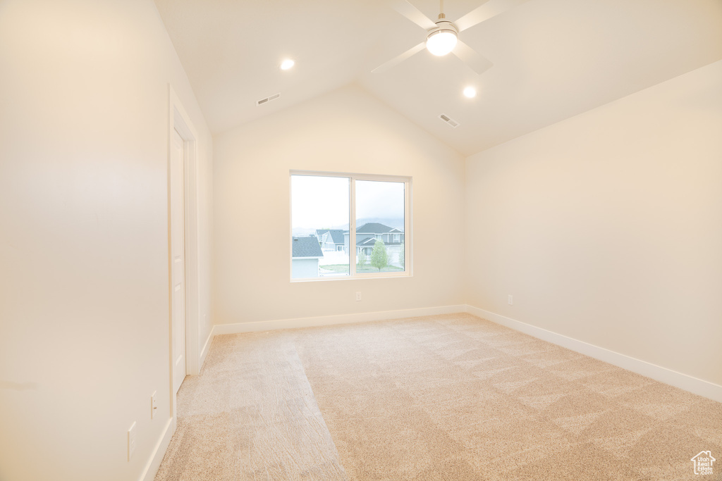 Empty room featuring light colored carpet, ceiling fan, visible vents, and vaulted ceiling