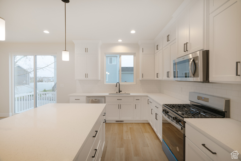 Kitchen featuring a sink, tasteful backsplash, stainless steel appliances, and light wood-type flooring