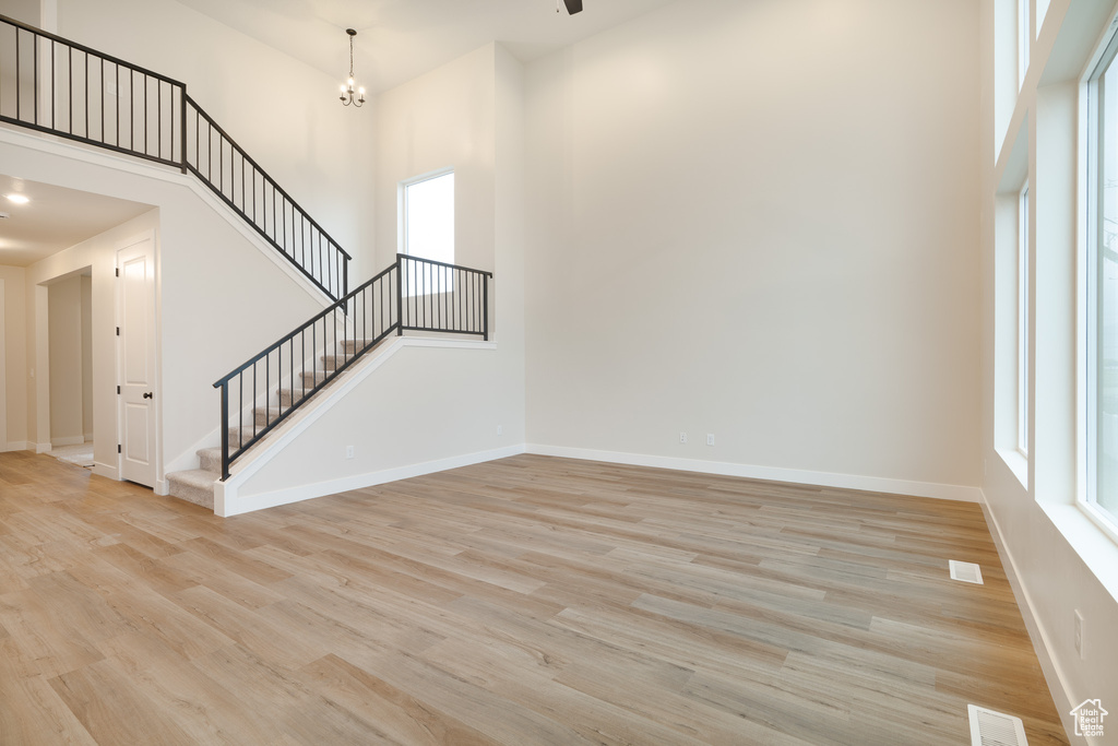 Unfurnished living room with stairs, a high ceiling, baseboards, and light wood finished floors