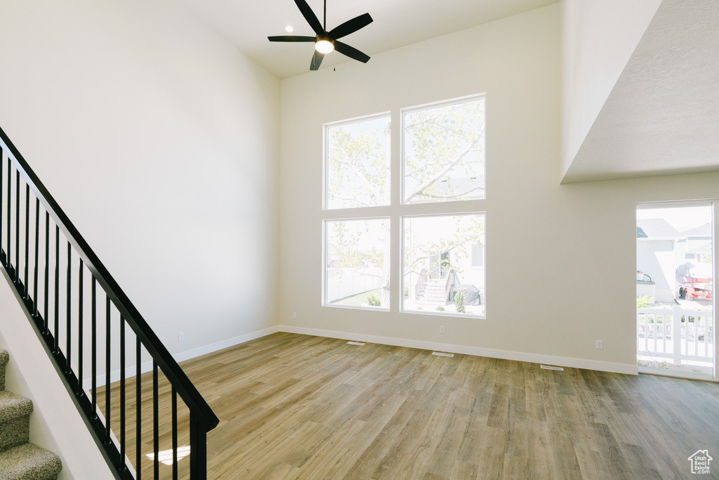 Unfurnished living room featuring baseboards, a ceiling fan, stairs, and wood finished floors