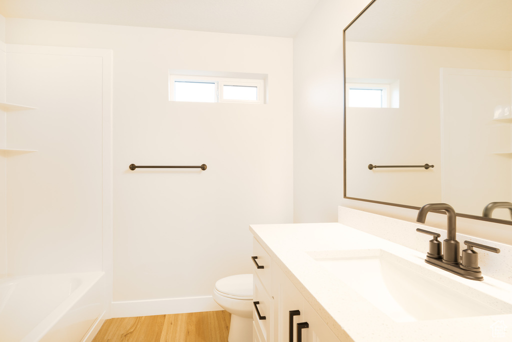 Full bathroom with baseboards, wood finished floors, a healthy amount of sunlight, and toilet