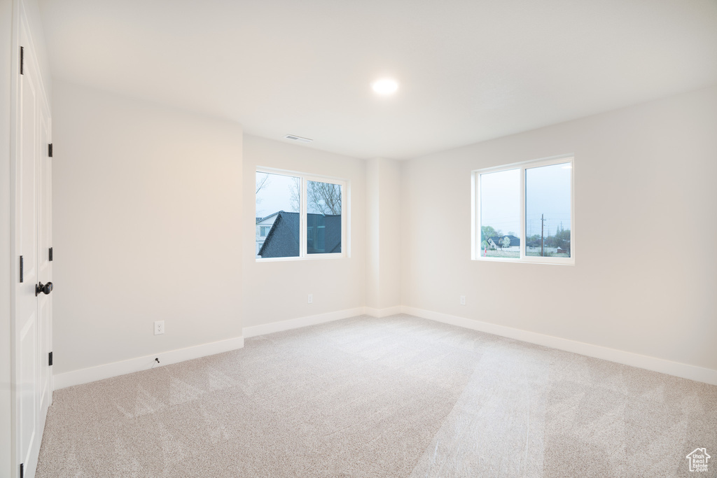 Spare room with baseboards, plenty of natural light, visible vents, and light carpet